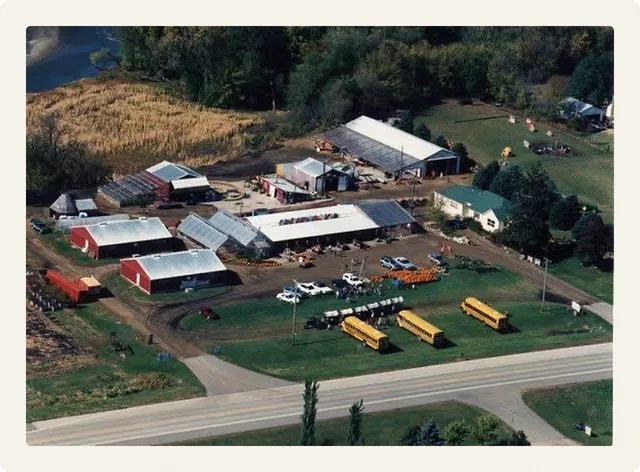 The family market seen from the air, with red barns, greenhouses and school buses