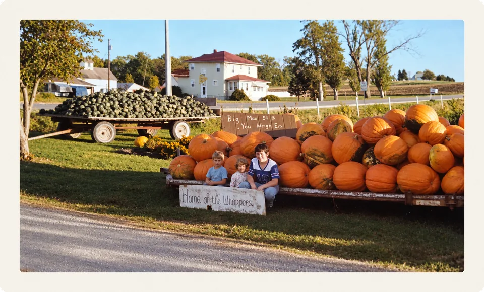 Todd, Troy and Tania at the family pumpkin stand, with a wagon of squash and the white farmhouse behind