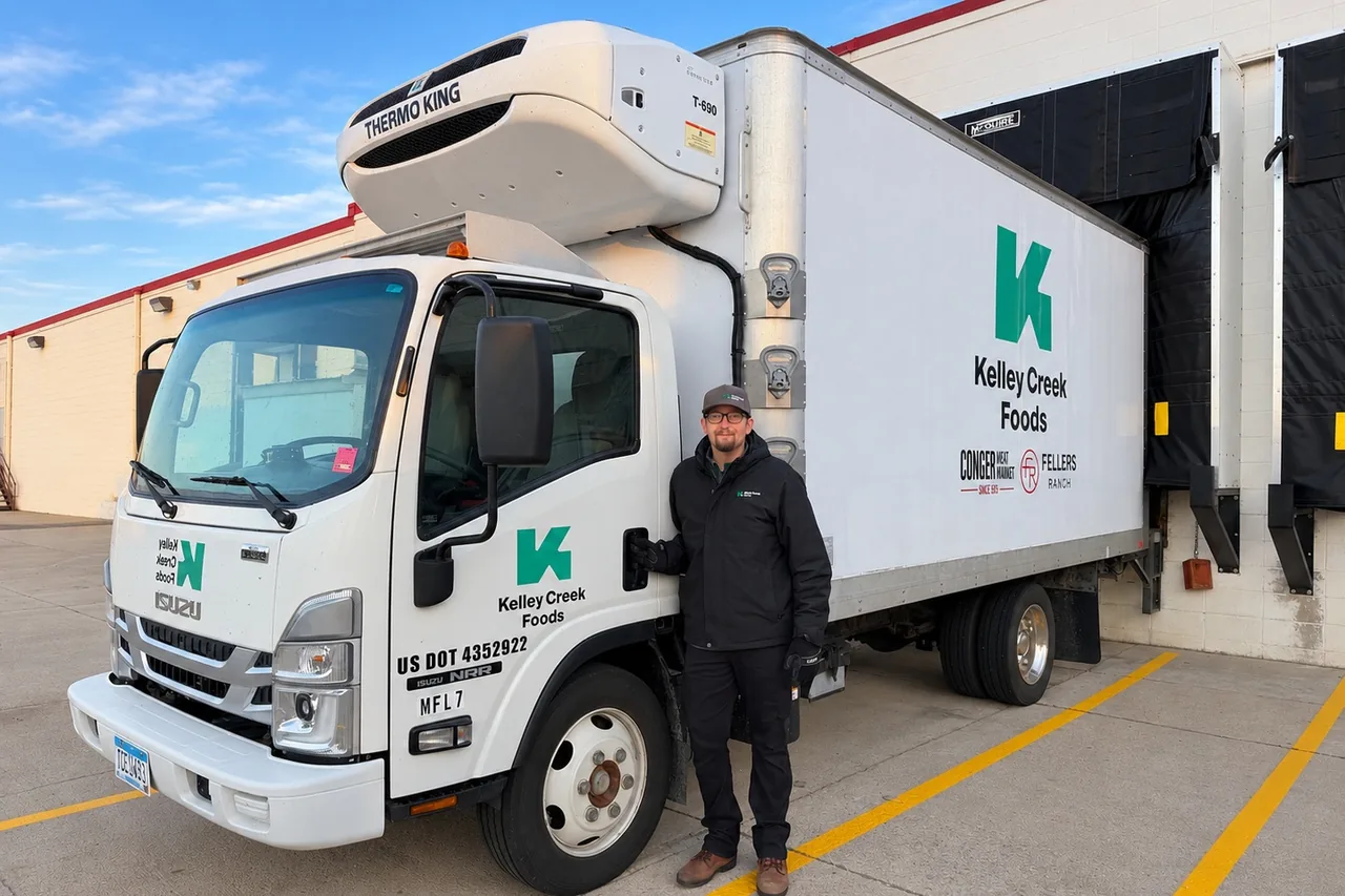 A Kelley Creek Foods refrigerated box truck at a loading dock, with a team member beside it
